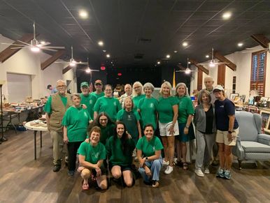 Group of people in green shirts posing indoors in a large room.