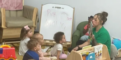 Kids watching a woman as she draws a design on a sheet of paper.