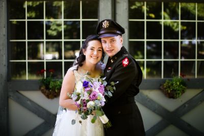 Bride in white dress holding flowers, groom in uniform smiling