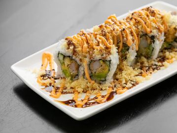 Sushi rolls with sauces and tempura flakes on a white plate.