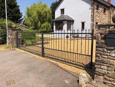 Black metal gate and stone fence in front of a country house.