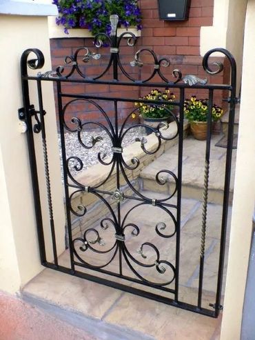 Decorative black wrought iron gate with floral designs at a garden entrance.