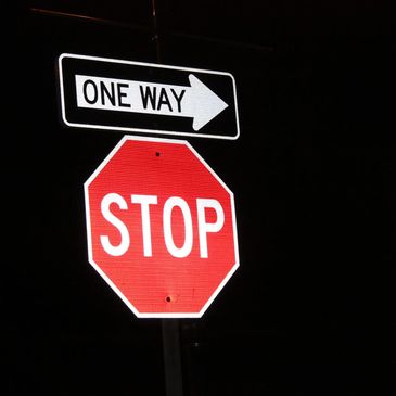 stop sign and one way sign illuminated aginst starkly contrasted black background