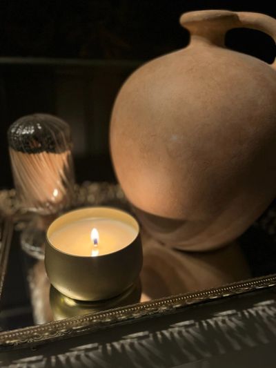 A lit candle, a beige clay pot, and matchsticks on a reflective surface.