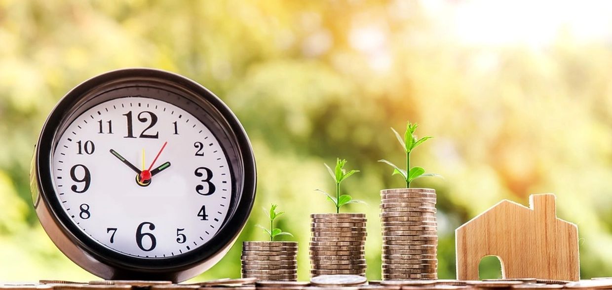 Clock, stacks of coins with growing plants, and a wooden house model.