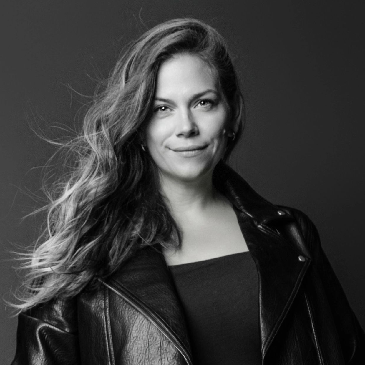 Black and white portrait of a woman with flowing hair in a leather jacket.