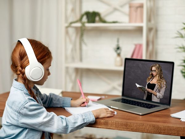A young girl with headphones having an education lesson online with a teacher