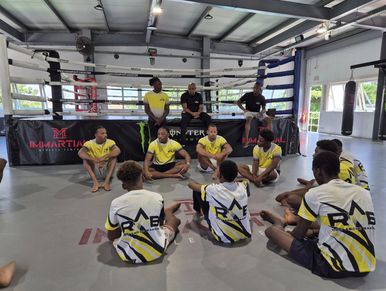 A group of martial artists sitting and kneeling in a gym with boxing ring.