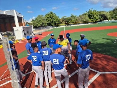 Youth baseball team gathers for a pre-game meeting on a sunny field.