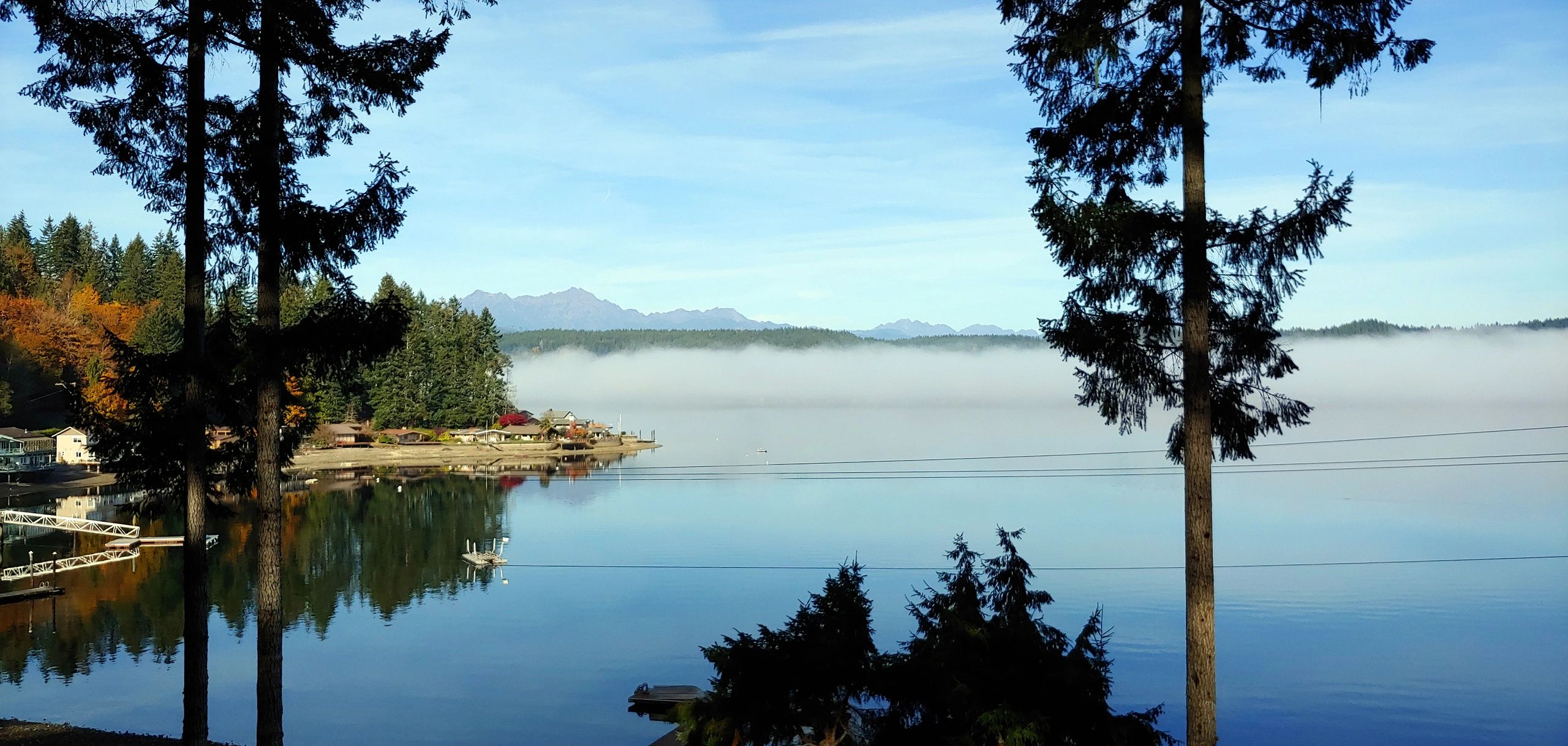 Calm lake reflecting trees and misty mountains under a clear sky.