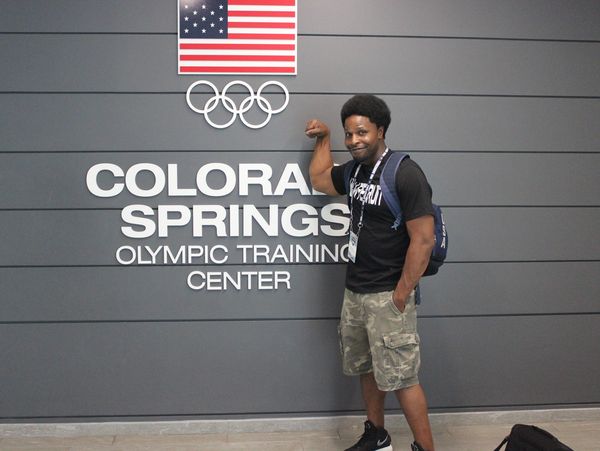Man flexes arm in front of Colorado Springs Olympic Training Center sign.