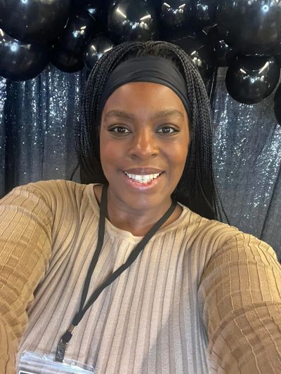 Smiling woman with braided hair taking a selfie in front of black balloons and a glittery backdrop.