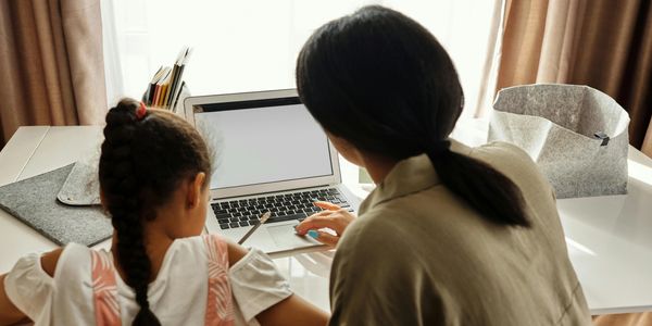 Woman helping a girl with homework using a laptop at a desk.