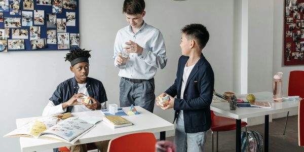 Three boys interacting in a classroom with books and puzzles.