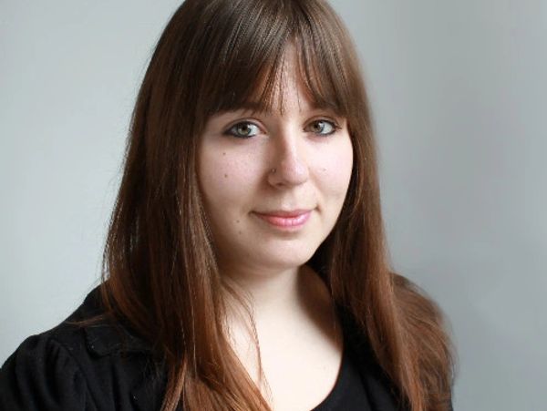 Portrait of a young woman with brown hair and bangs, wearing a black top.