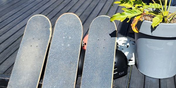 Three skateboards leaning against a wooden deck under a sunny sky.