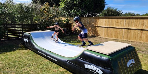 Two kids skateboarding on an inflatable ramp in a backyard.