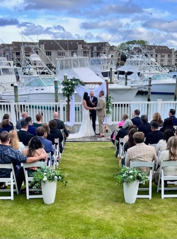 Couple exchanging vows at a waterfront wedding with boats in the background.