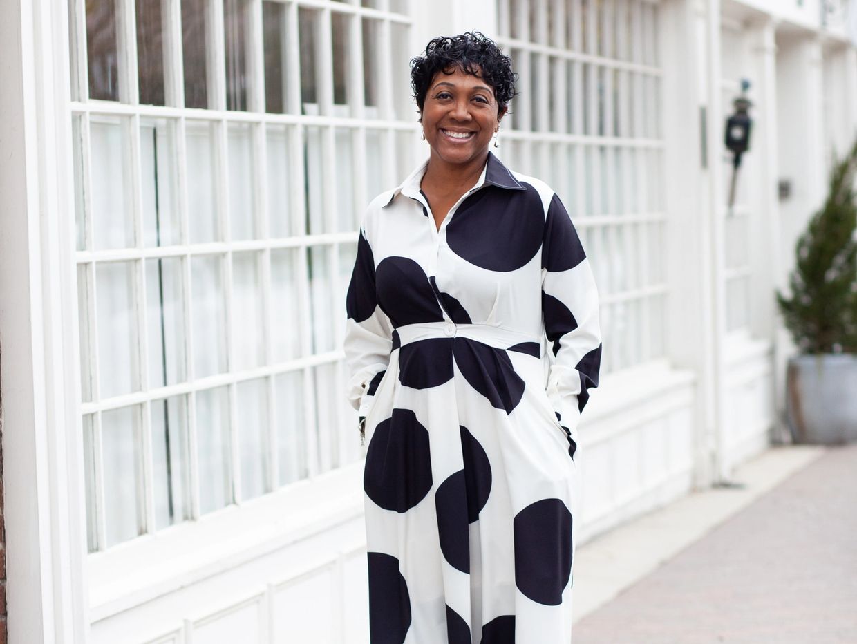 Woman in a black and white polka dot dress smiles outdoors.