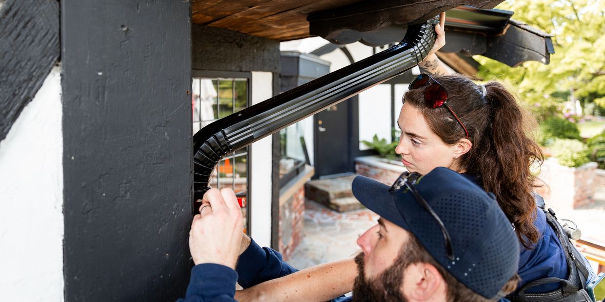 Two people inspecting a black rain gutter on a house.