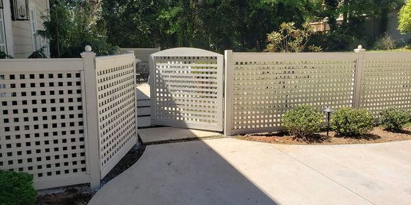 A white lattice fence and gate around a patio area with greenery.