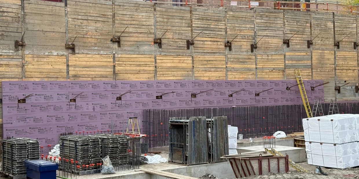 Construction site with concrete forms and insulation boards against a retaining wall.