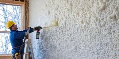Worker spraying foam insulation on interior wall.