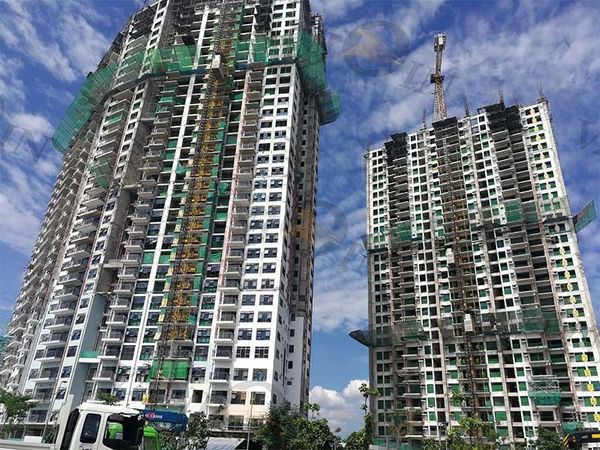 Two high-rise buildings under construction with cranes and scaffolding against a blue sky.