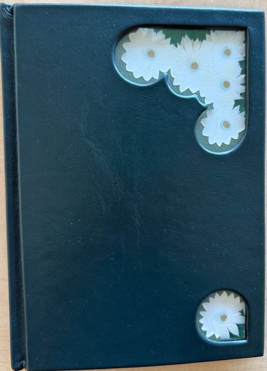 A dark green photo album with floral corner cutouts showing white daisies.