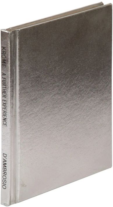 A shiny silver hardcover book titled 'Krome: A Further Experience' by D'Ambrosio.