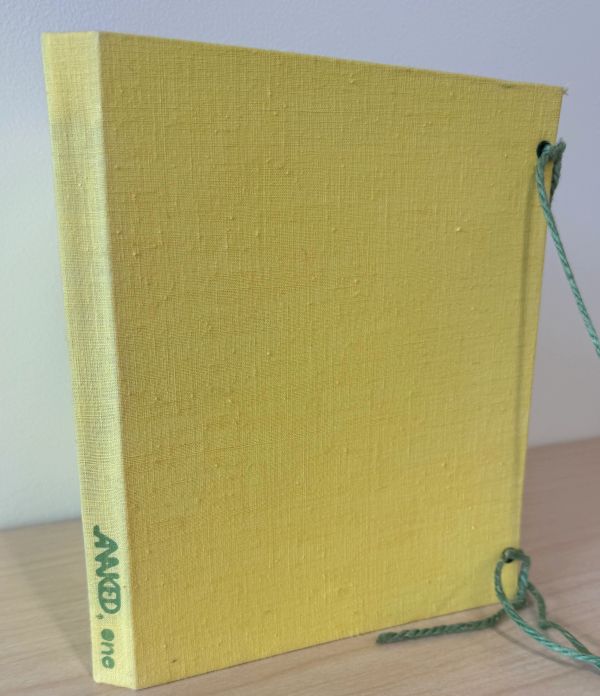 Yellow hardcover book with green string ties and textured surface.