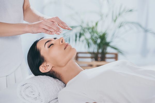 Cropped shot of calm young woman with closed eyes receiving reiki treatment above head