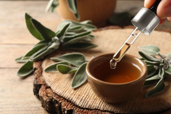 Woman dropping essential sage oil into bowl at wooden table