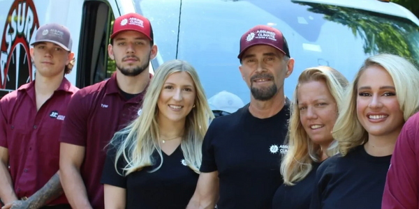 A group of six people posing in front of a vehicle wearing branded work shirts and caps.