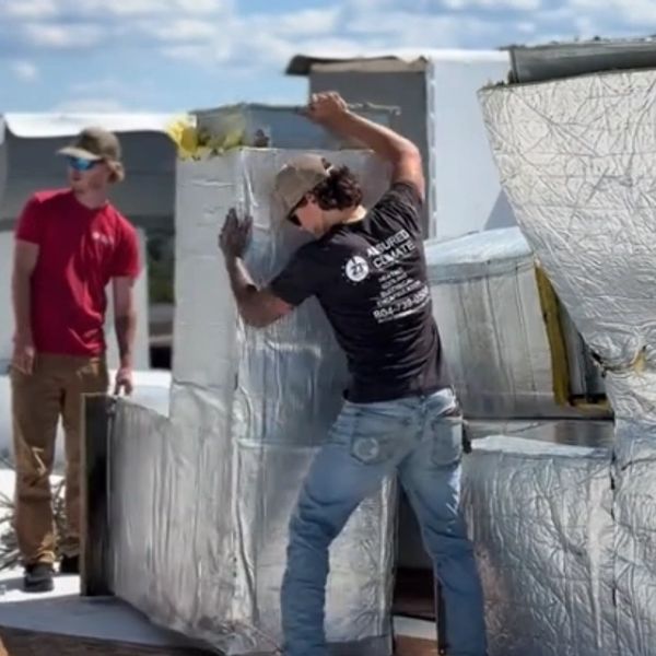 Workers installing reflective insulation on ductwork outdoors under a blue sky.
