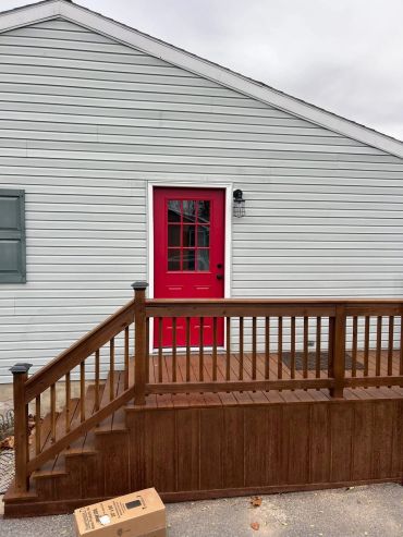 House with white siding and a red door with wooden railing.