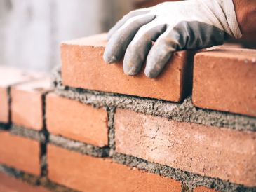 Hand laying bricks with mortar in construction work.