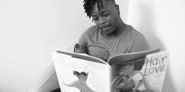 Black man reading "Hair Love" to a baby