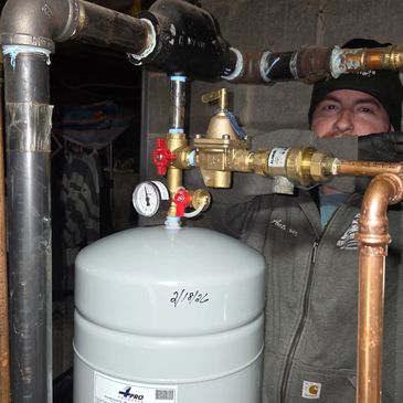 A plumber working on pipes and a pressure tank in a basement.