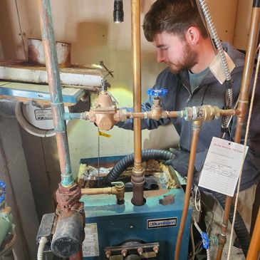 A technician inspecting a furnace with exposed pipes in a basement.