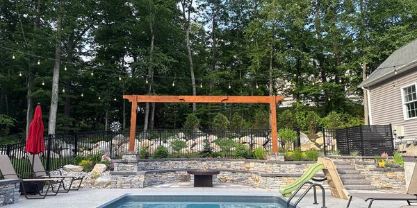 Backyard pool area with stone seating and wooden pergola.
