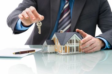 Man holding a key while clutching a miniature house beside a document