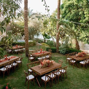 Outdoor garden dining setup with wooden tables, chairs, and string lights.