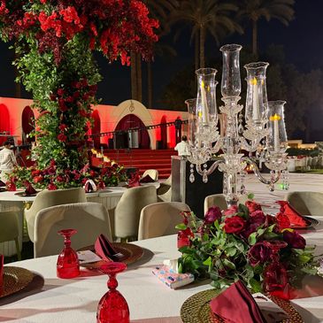 Elegant outdoor event setup with red and green floral decorations and candlelit chandelier.