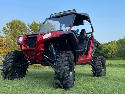 Red off-road ATV with large tires parked on grass under clear sky.