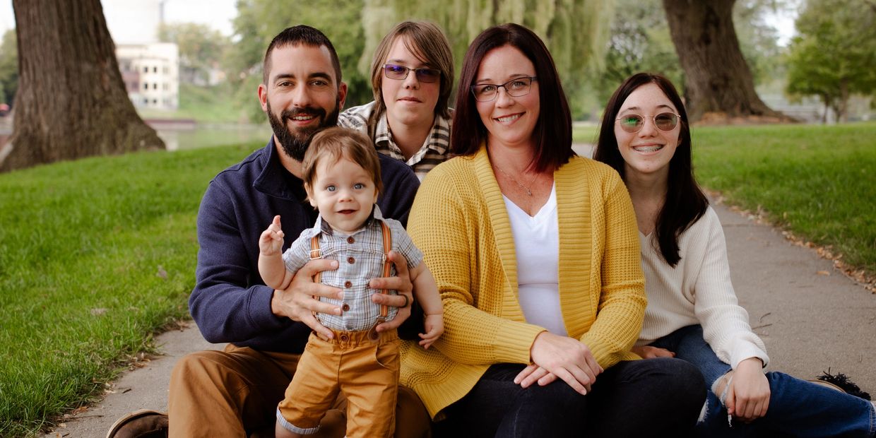 A happy family of five sitting on a blanket outdoors in a park.