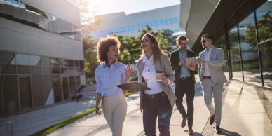 Four professionals walking and discussing outside a modern office building.