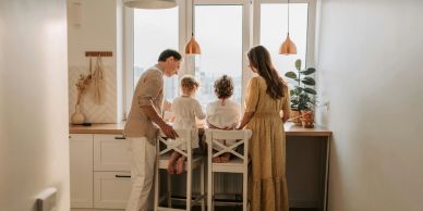 A family of four gathered around a kitchen counter with a bright window.