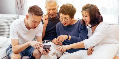 Four family members gathered around a smartphone on a couch.
