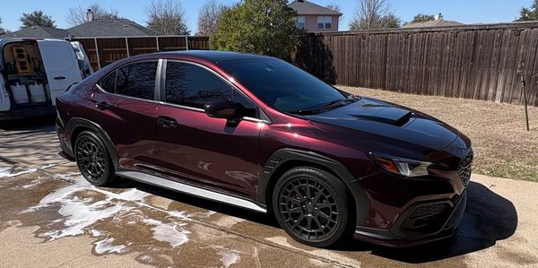 A shiny maroon sports sedan parked in a driveway on a sunny day.